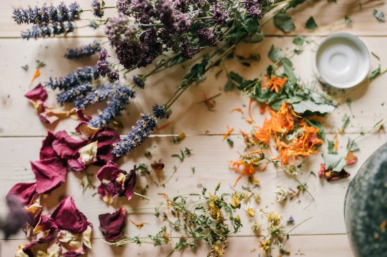 Assorted dried flowers and herbs scattered on a wooden table with a ceramic bowl.