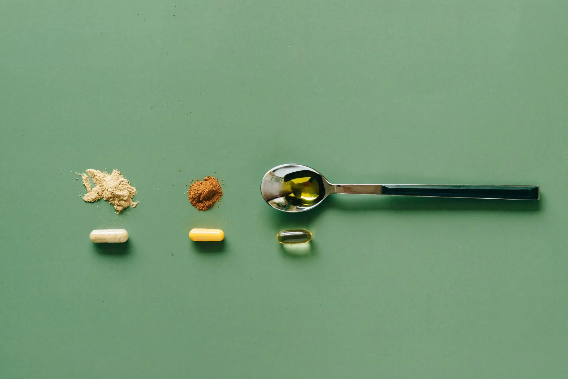 Top view of various supplements and powders on a green surface with a spoon.